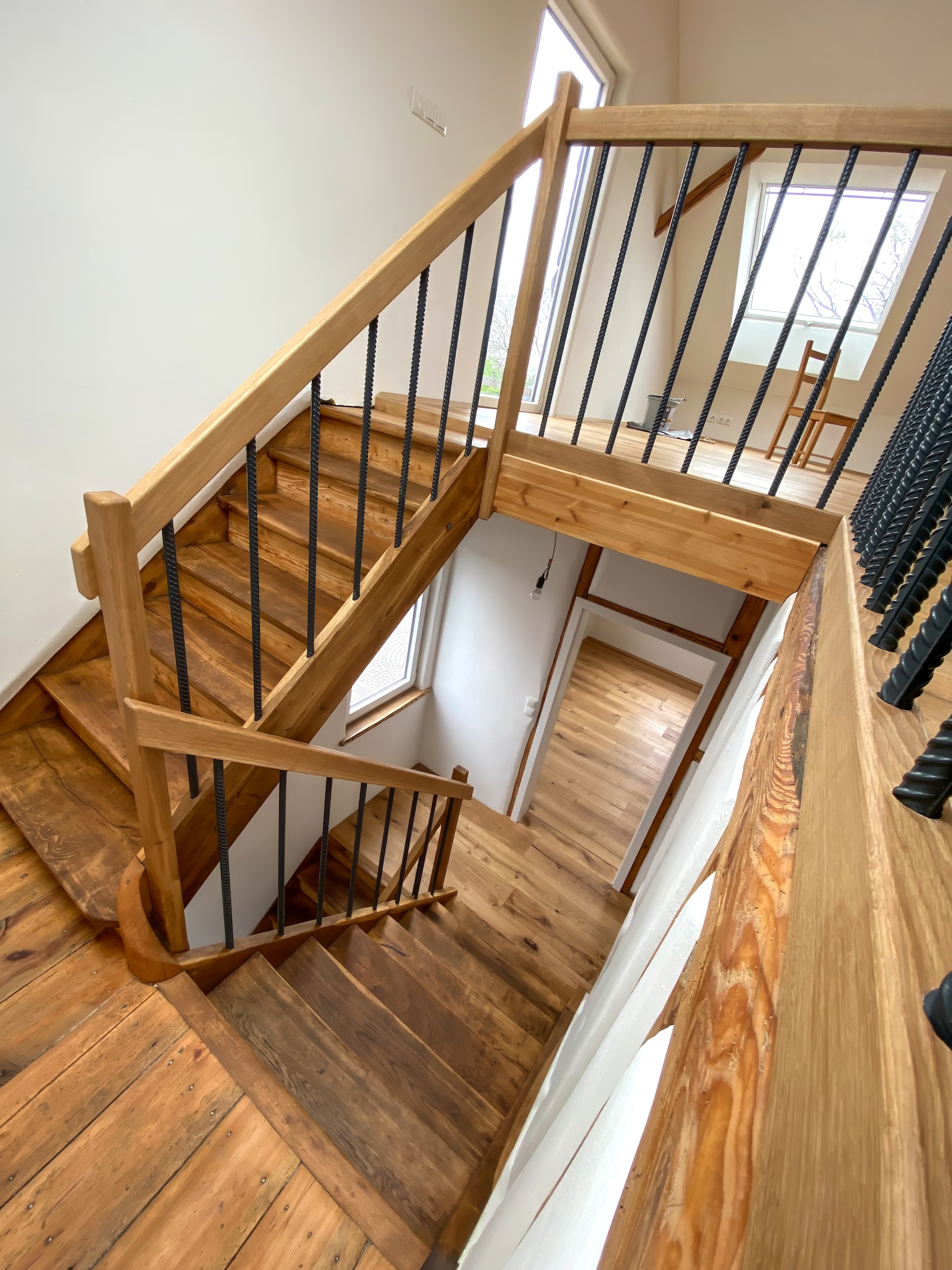 Moderne Holztreppe mit schwarzen Metallstäben im Geländer verbindet mehrere Etagen in einem hellen Innenraum.