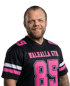 Mann mit Bart in schwarzem Trikot mit pinker Aufschrift "WALHALLA GYM" und der Nummer "85" lächelt.