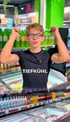 Junger Mann mit Brille und schwarzem T-Shirt mit Aufschrift "TIEFKÜHL" steht in einem Supermarkt.