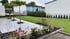 Moderner Garten mit grauer Fliesenterrasse, Rasenfläche, Blumenbeeten mit Hortensien und jungen Bäumen vor Wohngebäuden.