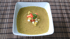 Grüne Suppe in einer weißen Schale mit Croutons, Paprika und Petersilie.