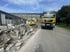 Gelber Witte LKW und Bagger stehen neben einem Schutthaufen vor einem Steingebäude auf einer Baustelle.