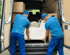 Zwei Männer in blauen Uniformen laden ein weißes Sofa in einen Transporter, um.