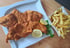 Goldbraunes Schnitzel mit Zitronenscheiben und Pommes Frites auf einem Holztisch.