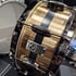 Goldene Snare-Drum von Piroth Drums mit schwarzem Mittelstreifen und verchromten Spannreifen.