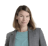 Eine Frau mit braunem Haar und grauer Jacke lächelt vor einem grünen Hintergrund.