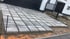 Neu verlegte, quadratische Gehwegplatten in Grau auf einer Garageneinfahrt vor einem modernen Haus mit schwarzem Zaun.