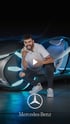 Ein Mann mit zerrissener Jeans und weißem T-Shirt hockt vor einem futuristischen Auto und macht Rock-Handzeichen.