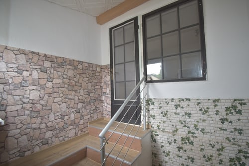 Treppe mit Holzstufen, Steinwand und Fenster mit schwarzem Rahmen.