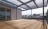 Geräumige Dachterrasse mit Holzfußboden, Metallgeländer und transluzentem Vordach.