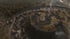 Aerial view of a large ancient hill fort with concentric earthworks and wooden structures surrounded by forest.