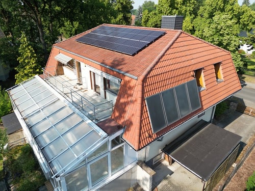 Haus mit rotem Ziegeldach, Solarpaneelen und einem verglasten Wintergarten.