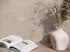 Beige Wand in Steinoptik mit Schattenspiel, Vase mit Trockenblumen und aufgeschlagenem Buch