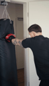 Ein Mann mit Tätowierungen schlägt mit einem roten Boxhandschuh auf einen schwarzen Boxsack.