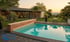 Ein Pool mit Holzeinfassung und einer modernen Villa im Hintergrund bei Sonnenuntergang.