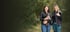 Lächelnde junge Frau sitzt auf einem Waldweg und hält einen schwarz-weißen Border Collie Welpen im Arm.