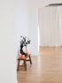 Holzbank mit Buddha-Figur, rosa Kerzen und Vase mit Zweigen in einem hellen Raum.
