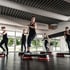 Fünf Frauen in schwarzer Sportkleidung trainieren auf Steppern in einem Fitnessstudio.