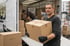 Mann trägt Umzugskarton, anderer Mann im LKW lädt Kartons aus. Ein Karton ist mit "Küche" beschriftet.