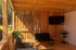 Holzterrasse mit schwarzem Sofa, Sessel, Couchtisch, Fernseher und einem geflochtenen Herz an der Wand.