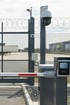 Sicherheitszaun mit Stacheldraht, Überwachungskameras und einer Parkplatzschranke mit Kartenlesegerät.