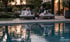 Ein Paar entspannt auf Sonnenliegen an einem Pool bei Sonnenuntergang; Logo von Mayr Schwimmbad-Technik unten rechts.