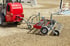 Ein roter Weidemann 1280 Traktor mit einem Anbaugerät ebnet einen Sandreitplatz.