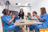 Healthcare professionals in blue and green scrubs clapping around a conference table with one woman standing.