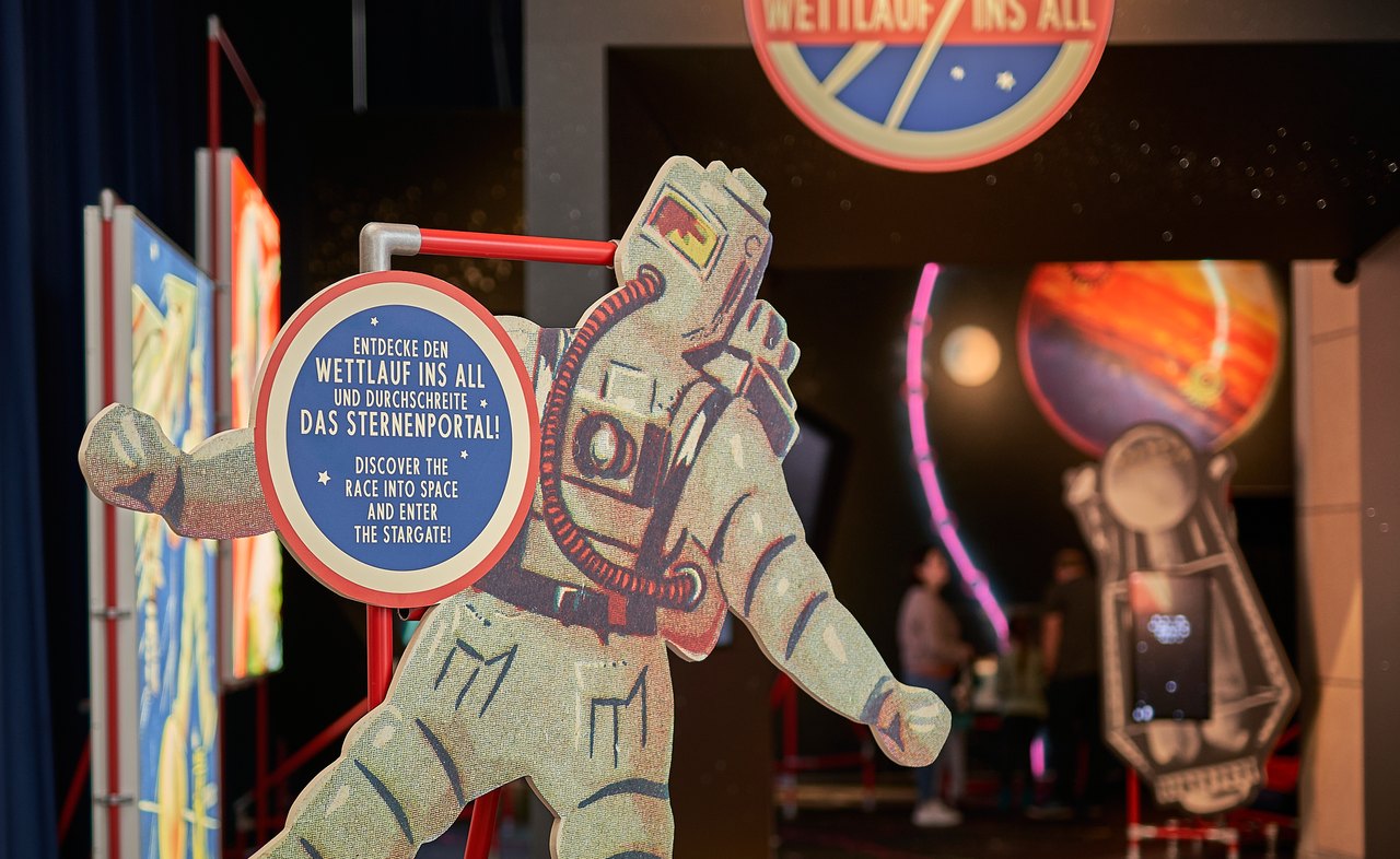 ‚Entdecke den Wettlauf ins All und durchschreite das Sternenportal!‘ – Retro-Astronaut am Eingang