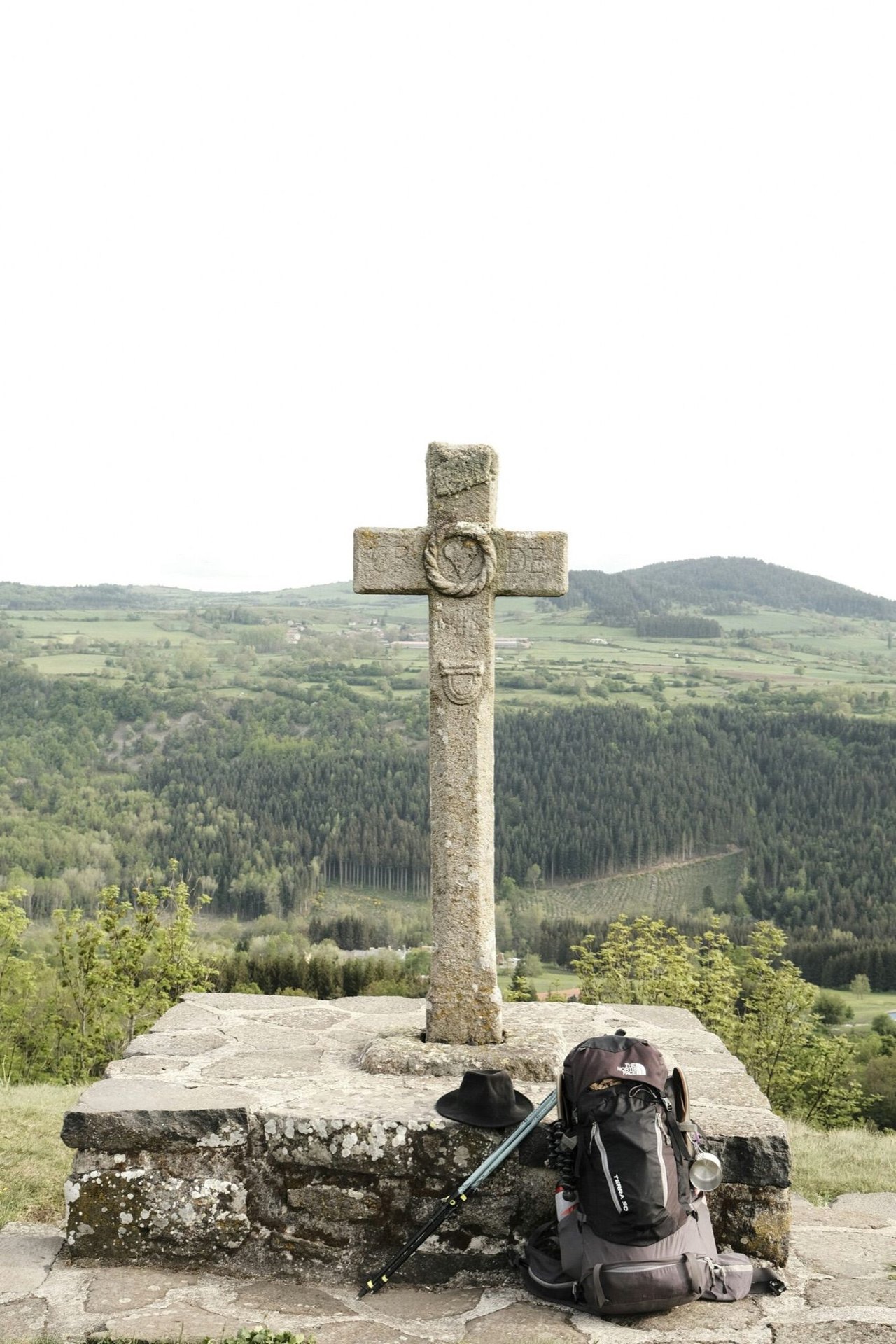 Steinernes Kreuz auf einer Anhöhe, davor ein abgestellter Rucksack