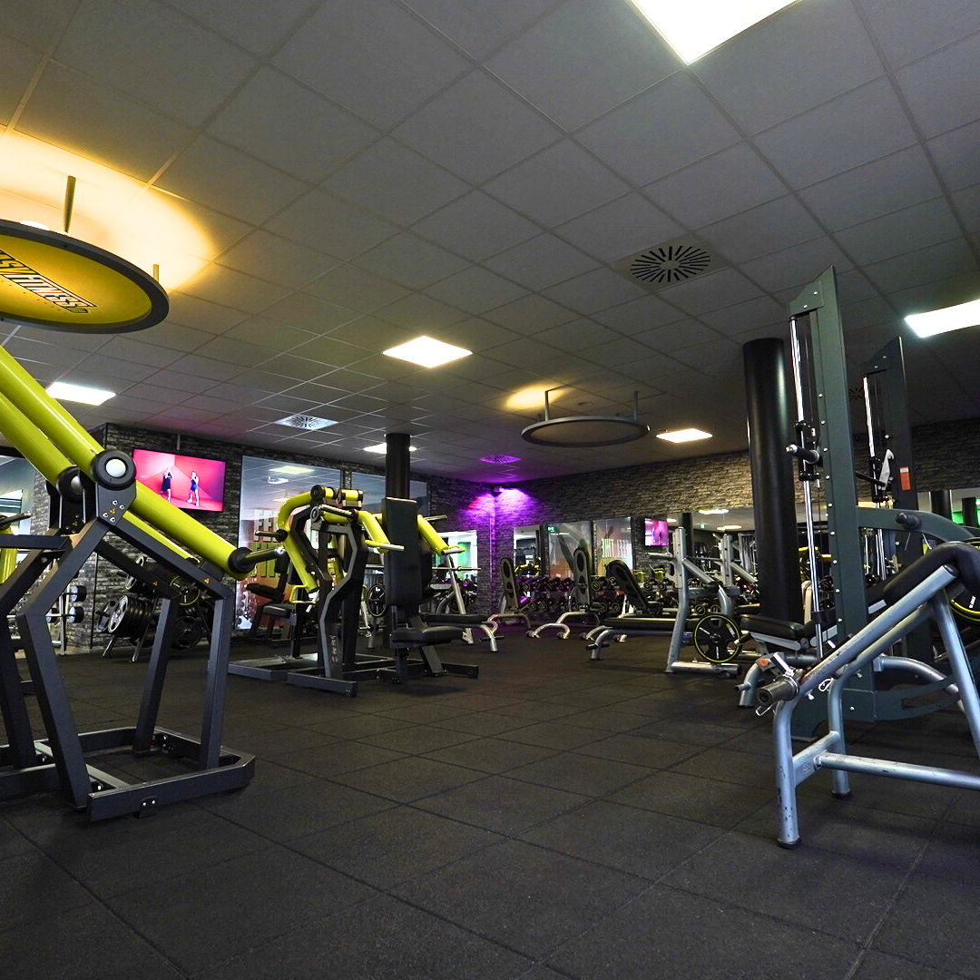 Fitnessstudio mit verschiedenen Trainingsgeräten und schwarzen Gummiböden.