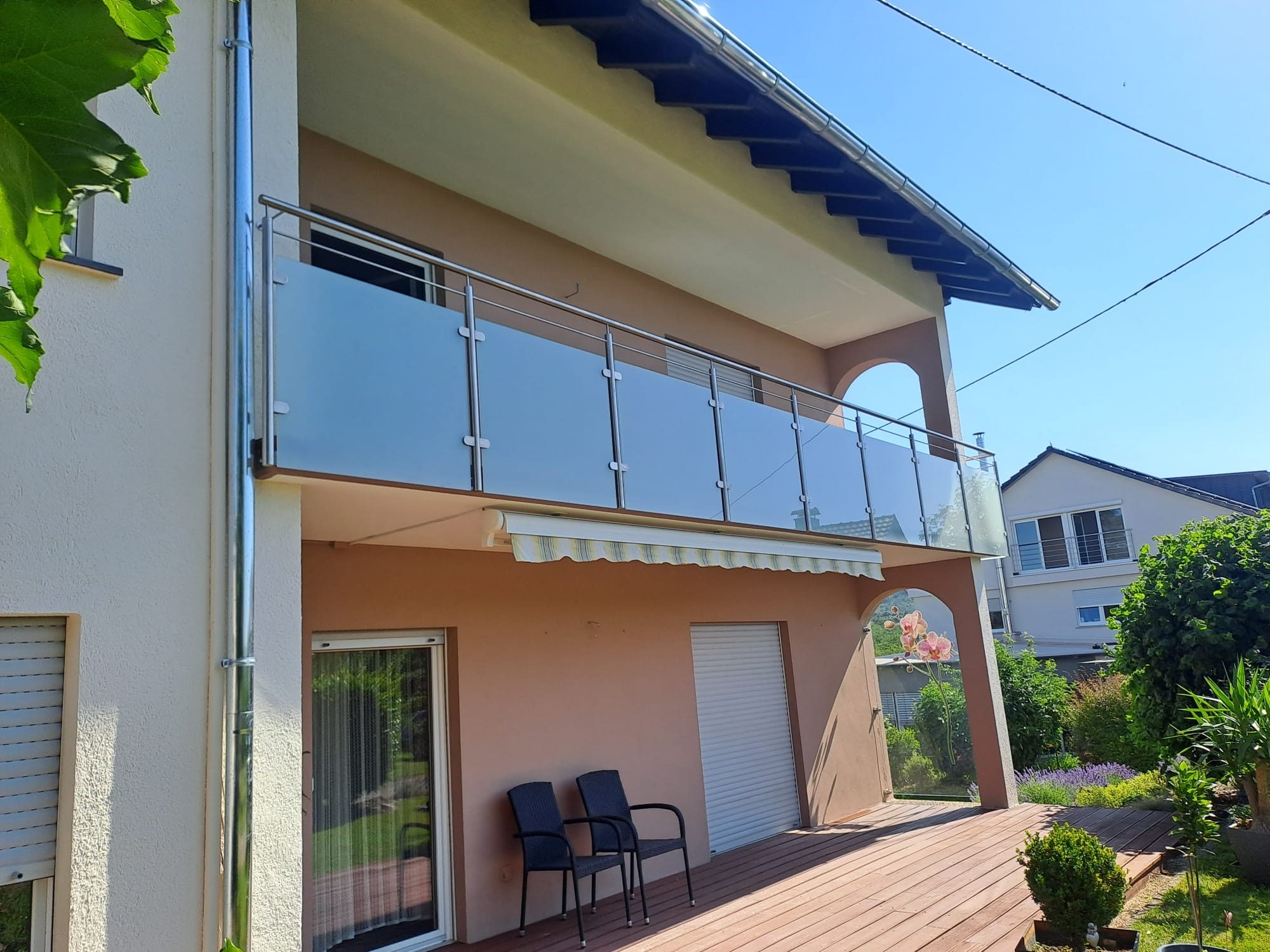 Balkon mit Milchglas-Geländer und Edelstahlpfosten über einer Holzterrasse