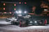 Ein beleuchteter Pistenbully auf Schnee bei Nacht vor einem Gebäude mit Lichtern.