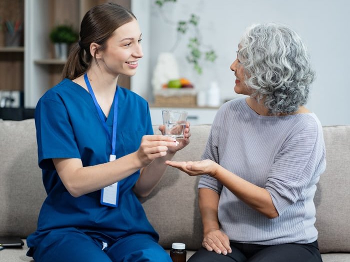 Pflegekraft reicht einer Seniorin ihre Medikamente