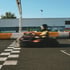 Ein Go-Kart fährt schnell über eine Ziellinie mit einem schwarz-weiß karierten Muster auf dem Asphalt.