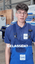 Ein junger Mann mit Brille und blauer Arbeitskleidung steht in einer Werkstatt. Text: GELASSEN?