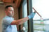 Mann in blauem Poloshirt und Handschuhen reinigt ein Fenster mit einem Abzieher.