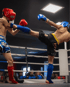 Zwei Kickboxer in Schutzkleidung kämpfen im Ring, einer tritt mit dem Bein.