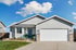 Light gray single-story house with white garage door, small front porch, and green lawn under blue sky.