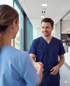 Zwei medizinische Fachkräfte in blauer Uniform geben sich in einem hellen Krankenhausflur die Hand.