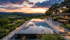 Infinity-Pool reflektiert orangefarbenen Sonnenuntergang über grünen Hügeln und Weinbergen.
