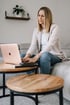 Eine blonde Frau sitzt auf einem Sofa und tippt auf einem roségoldenen Laptop.