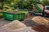 Ein LKW kippt Sand neben einem grünen Container "Fa. Joh. Onken" und vier Erdhaufen.