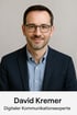 David Kremer, Digitaler Kommunikationsexperte, lächelt und trägt eine Brille, ein blaues Hemd und einen dunkelblauen Blazer.
