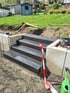 Vierstufige Außentreppe aus dunklem Stein auf einer Gartenbaustelle mit Betonmauern und Absperrband.