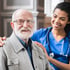 Ein lächelnder älterer Mann mit Brille und ein dunkelhäutiger Pfleger mit blauem Kittel und Stethoskop.
