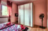 Schlafzimmer mit Doppelbett, weißem Kleiderschrank, Fenster mit roten Vorhängen und Ventilator.