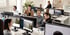 Mehrere Personen arbeiten konzentriert an Computern in einem modernen Büro mit weißen Schreibtischen.
