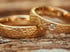Zwei goldene Eheringe mit gehämmerter Oberfläche auf Holzgrund, ein Ring mit eingefasstem Diamanten.