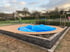 Ein runder Pool mit blauer Abdeckung auf einer Holzterrasse mit Steineinfassung in einem Garten.